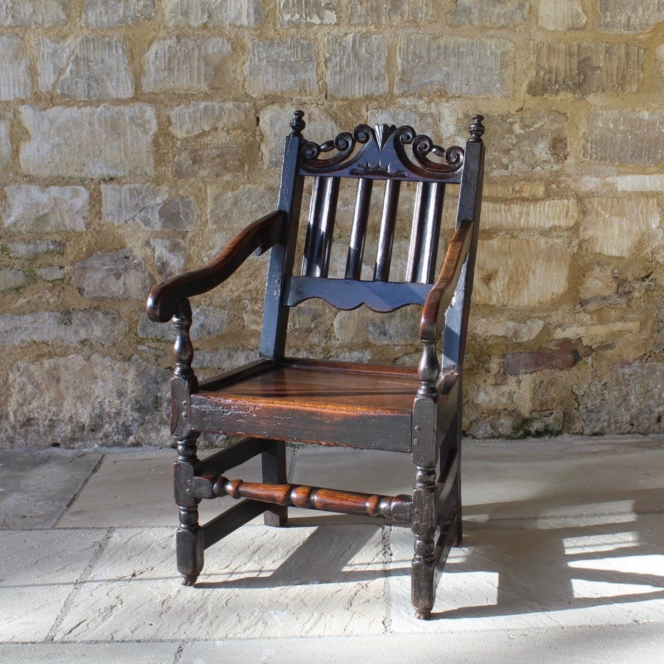 good-late-C17th-English-joined-oak-armchair-slat-back-good-angle-rake-particularly-comfortable-features-highly-decorative-well-carved-crest-rail-shaped-mid-rail-considerable-aesthetic-appeal-down-swept-arms-nicely-turned-supports-boarded-seat-turned-square-legs-stretchers-good-solid-condition-excellent-colour-beautifully-contrasting-black-gold-tones-for-sale-damon-blandford-antiques-stroud-stow-on-the-wold-early-oak-cotswold-country-house